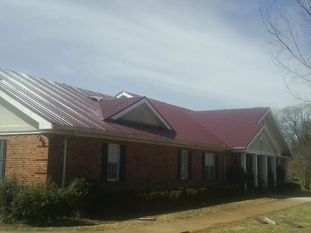 Red metal roof with gabled entries on a long brick building, from a Hail Damage Roof Repair job in Capron